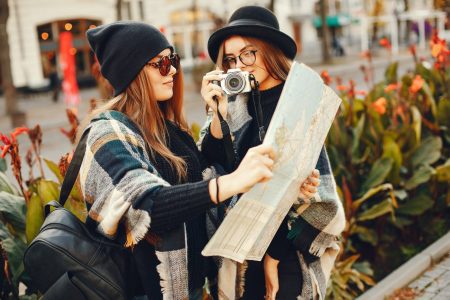 Two young stylish girls travel in an unknown city with a map